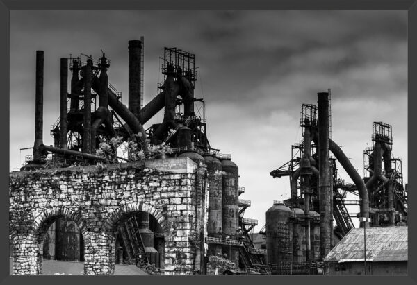 Rusted smoke stacks behind a crumbling stone wall.